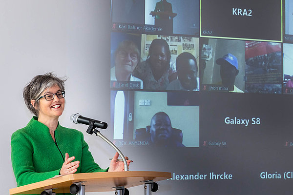 Birgit Mock, Mitglied des AGIAMONDO-Vorstands und Geschäftsführerin des Hildegardis-Vereins, gibt die Gewinnerin bekannt. Die Nominierten sind im Hintergrund per Video zugeschaltet.