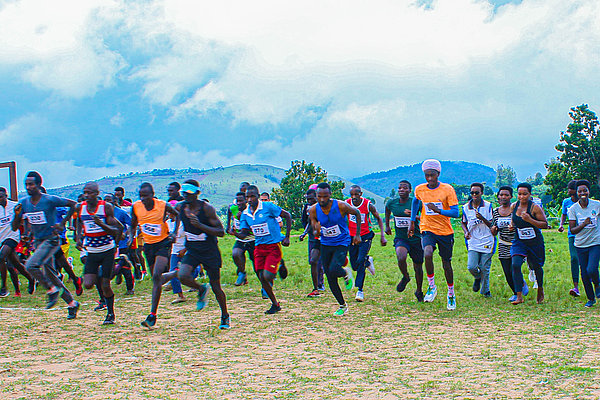 Das Startsignal für den Geländelauf "Course pour la Paix" an der weißen Torlinie des Fußballfelds von Bururi ist ertönt. Alle Läufer*innen des Friedenslaufs sprinten Richtung Dorfplatz, dem Ziel des Wettlaufs.