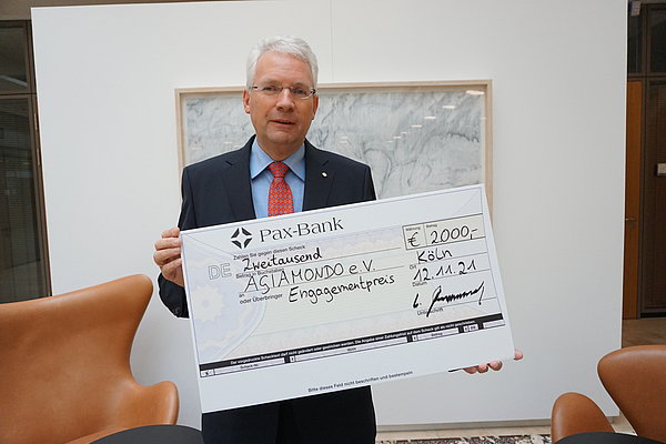 Wolfgang Altenrath, Regionaldirektor Köln der Pax-Bank eG, präsentiert den Scheck über 2.000 Euro Preisgeld. 