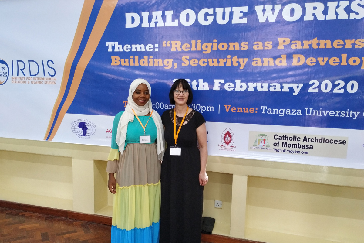 Ulrike Hanlon, ZFD-Teamleiterin bei AGIAMONDO, mit ihrer kenianischen Gastgeberin Warde Zighe (links) vor einem Plakat zur Ankündigung des achttägigen Exposure- und Dialogprogramms. Dieses fand in Kooperation mit AGIAMONDO im Februar 2020 in Kenia statt.